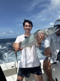 A young angler proudly displaying a large King Mackerel while fishing offshore, with a scenic ocean backdrop.