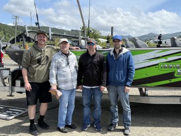 Four anglers posing in front of a vibrant green fishing boat, showcasing a sunny day at the dock.