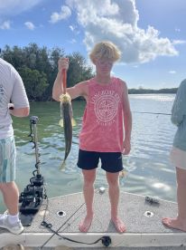 A young angler proudly displaying a large fish while fishing from a boat in a scenic coastal environment.