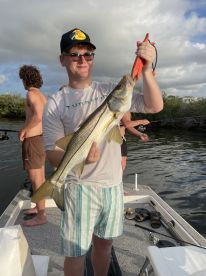 A young angler proudly displaying a Snook while fishing on a boat, surrounded by friends in a scenic waterway.