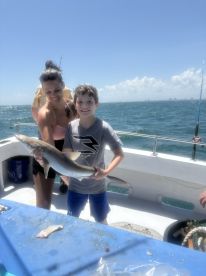 A young boy proudly holding a shark while fishing with family on a boat, showcasing a fun day on the water.