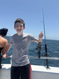 A young angler joyfully displaying a caught fish while fishing on a boat, enjoying a sunny day at sea.