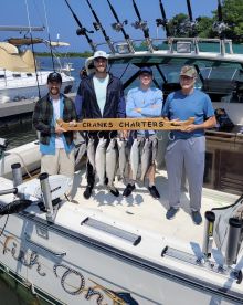 A group of anglers proudly displaying their catch of several trout on a charter boat named 'Fish On' after a successful fishing trip.