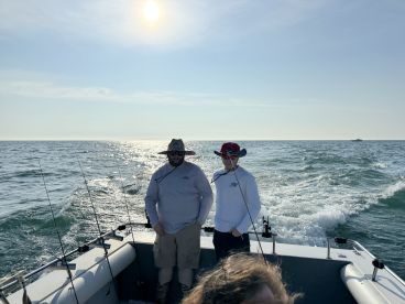 Two anglers enjoying a sunny day on the water aboard a fishing boat, with fishing rods ready for action.
