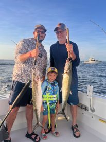 A family fishing trip showcasing a young boy and two adults proudly holding large King Mackerel on a boat, with a beautiful ocean backdrop.