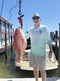 An angler proudly displaying a large Red Snapper at the dock, showcasing a successful fishing trip.
