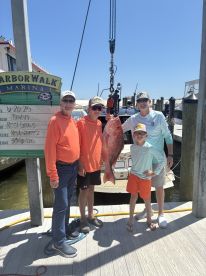 A family proudly displays a large Red Snapper caught during their fishing trip at Harborwalk Marina, showcasing a sunny day and a successful catch.