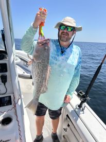 An angler proudly displaying a large Grouper while fishing on a boat in open waters.