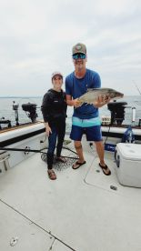 Two anglers proudly displaying a large fish on a boat during a fishing trip, showcasing a successful catch in a scenic water environment.