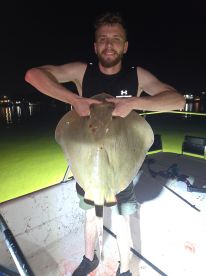 Angler proudly displaying a large stingray caught during a night fishing trip, showcasing the excitement of fishing under the stars.