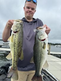 A young angler proudly displaying two large Largemouth Bass at a marina, showcasing a successful day of freshwater fishing.