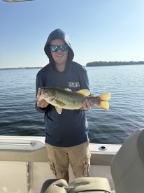 Angler proudly displaying a large Largemouth Bass while fishing on a serene lake, showcasing a sunny day and a well-equipped boat.