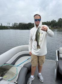 An angler proudly displaying a large Largemouth Bass while fishing from a pontoon boat on a calm lake.