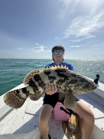 Young angler proudly displaying a large Goliath Grouper while fishing in open waters.