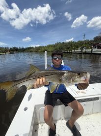 A young angler proudly displaying a Snook while fishing from a boat in a scenic waterway.
