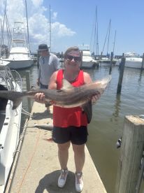 A proud angler displaying a large shark at the dock, showcasing a successful fishing trip in a marina setting.