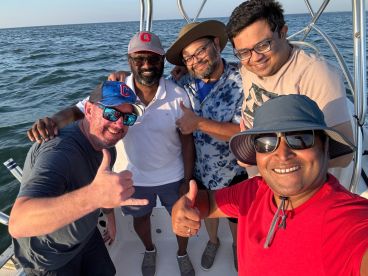 Group of friends enjoying a fishing trip on a boat, smiling and posing for a selfie against the backdrop of the water.