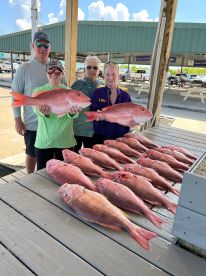 A family proudly displaying their catch of Red Snapper at a fishing dock, showcasing a successful day on the water.