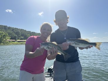 Two anglers proudly displaying their catches of Largemouth Bass while enjoying a sunny day on the water.