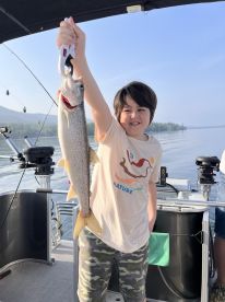 A young angler proudly displaying a caught Lake Trout while fishing on a calm lake, showcasing the excitement of a successful fishing trip.