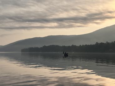 A serene morning scene featuring a fishing boat on calm waters, surrounded by misty mountains, perfect for a tranquil fishing experience.