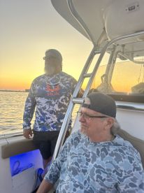 Two anglers enjoying a sunset view from the interior of a boat, showcasing a relaxed fishing atmosphere.