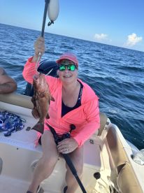 An angler proudly displaying a large Grouper while fishing on a boat in open waters.