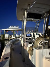 Interior view of a modern fishing boat's helm at dusk, showcasing the seating and control panel, with a marina in the background.