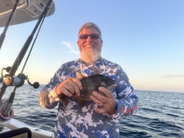 An angler proudly displaying a Black Drum caught during a sunset fishing trip on a boat.