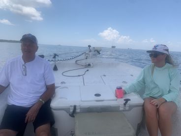 Two anglers relaxing on the boat, enjoying a calm day on the water, with a scenic backdrop of the Gulf Coast.