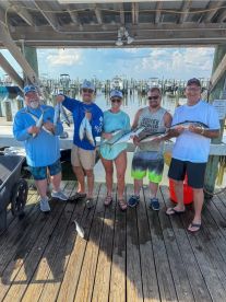 A group of five anglers proudly displaying their catch of Spanish Mackerel at the dock after a successful fishing trip.