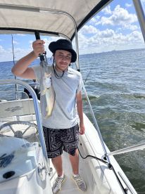 A young angler proudly displaying a caught fish while aboard a boat in a scenic fishing environment.