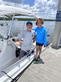 A smiling adult and child pose together on the side of a fishing boat at the dock, showcasing a family-friendly fishing environment.