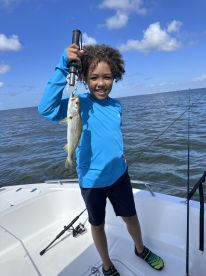 A young angler proudly displaying a caught fish while fishing on a boat in open waters.