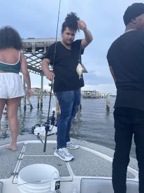 A young angler proudly displaying a caught fish while fishing from a boat, surrounded by family members in a scenic waterway.