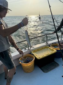 A young angler reeling in a fish during a vibrant sunset fishing trip on a charter boat.