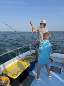 A young angler is reeling in a fish while another child observes on a fishing charter in open waters.