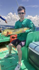 An angler proudly displaying a vibrant Mahi Mahi while seated on a fishing boat, enjoying a sunny day on the water.