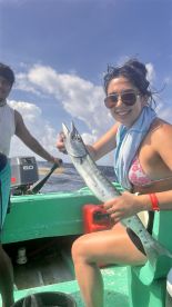 A young woman proudly displaying a Barracuda while fishing on a small boat, enjoying a sunny day on the water.