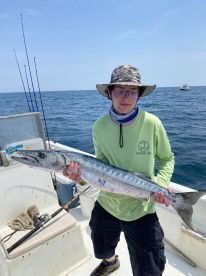 Young angler proudly displaying a large Barracuda while fishing offshore, showcasing a successful day on the water.
