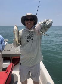 An angler proudly displaying a Speckled Trout while fishing on a boat in open waters.