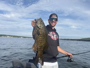 A proud angler displaying a large Smallmouth Bass while fishing on a serene lake, showcasing a perfect day for fishing.