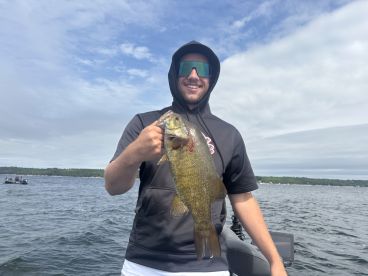 An angler proudly displaying a large Smallmouth Bass while fishing on a scenic lake, showcasing a successful day on the water.
