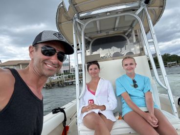 A group of three individuals enjoying a day on a center console boat, with a scenic waterfront in the background.