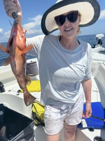An angler proudly displaying a large Grouper while fishing on a boat in sunny waters.
