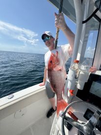 Angler proudly displaying a large Red Snapper while fishing offshore, showcasing a sunny day on the water.