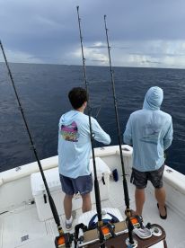 Two young anglers preparing to cast their lines while deep-sea fishing on a charter boat, surrounded by a vast ocean under a cloudy sky.