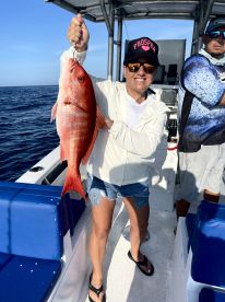An angler proudly displaying a vibrant Red Snapper aboard a fishing boat, showcasing a successful deep-sea fishing trip.