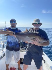 Two anglers proudly displaying a large Amberjack on a fishing charter in open waters.