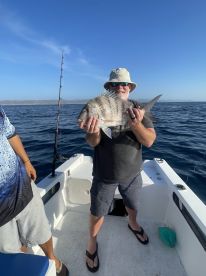 An angler proudly displaying a large Snapper while fishing on a boat in clear blue waters.